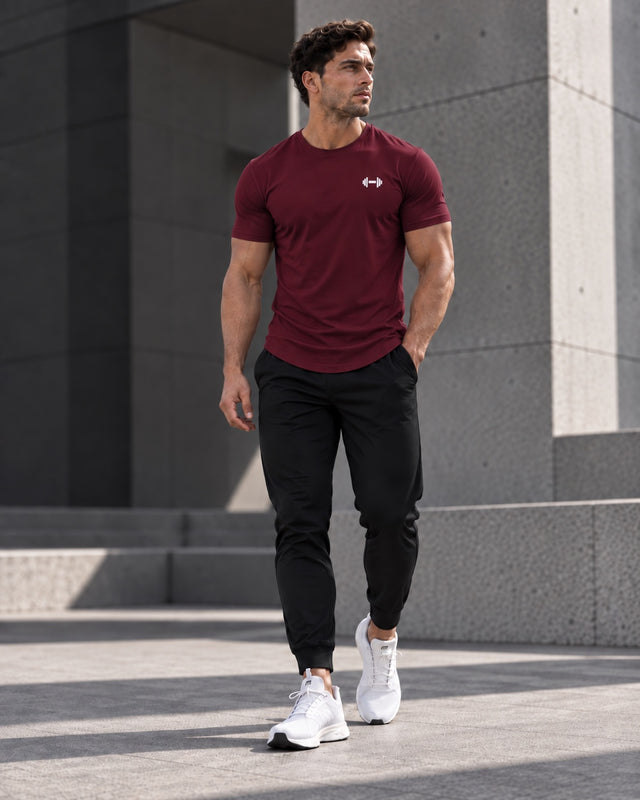 Form Muscle Tee in Burgundy, full-body walking view showing the curved hem, black joggers and white sneakers.