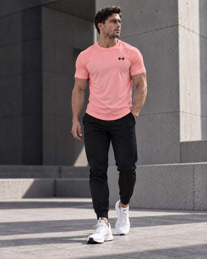 Form Muscle Tee in Coral, full-body walking view showing the curved hem, black joggers and white sneakers.