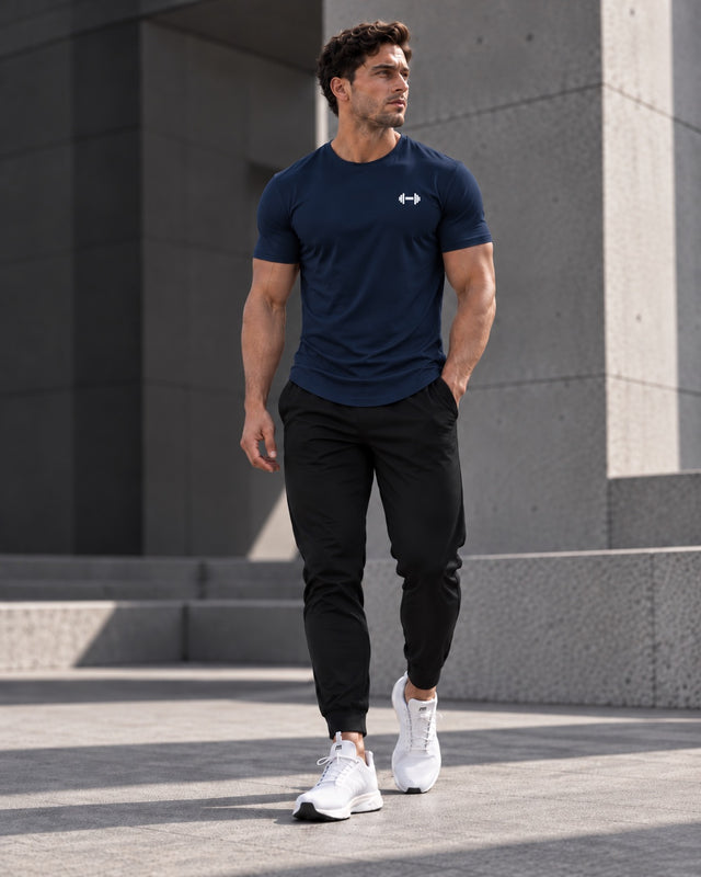 Form Muscle Tee in Navy, full-body walking view showing the curved hem, black joggers and white sneakers.